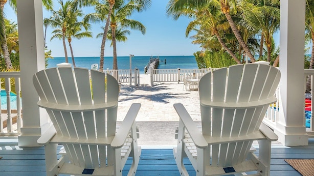 Two Adirondack chairs facing a beach with palm trees and a pier. - Turtle Crawl on Long Key Oceanfront Beachfront with dock and pool (Long Key)