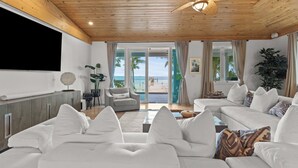 A spacious living room with a large sofa, a television, and a view of the beach. - Turtle Crawl on Long Key Oceanfront Beachfront with dock and pool (Long Key)