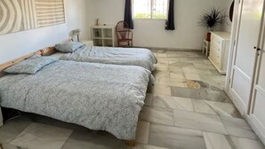 Un dormitorio con dos camas, una silla, un aparador y una ventana con cortinas.