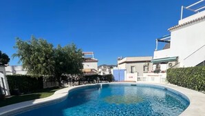 Una piscina con borde curvo, rodeada por un muro blanco y un patio empedrado.