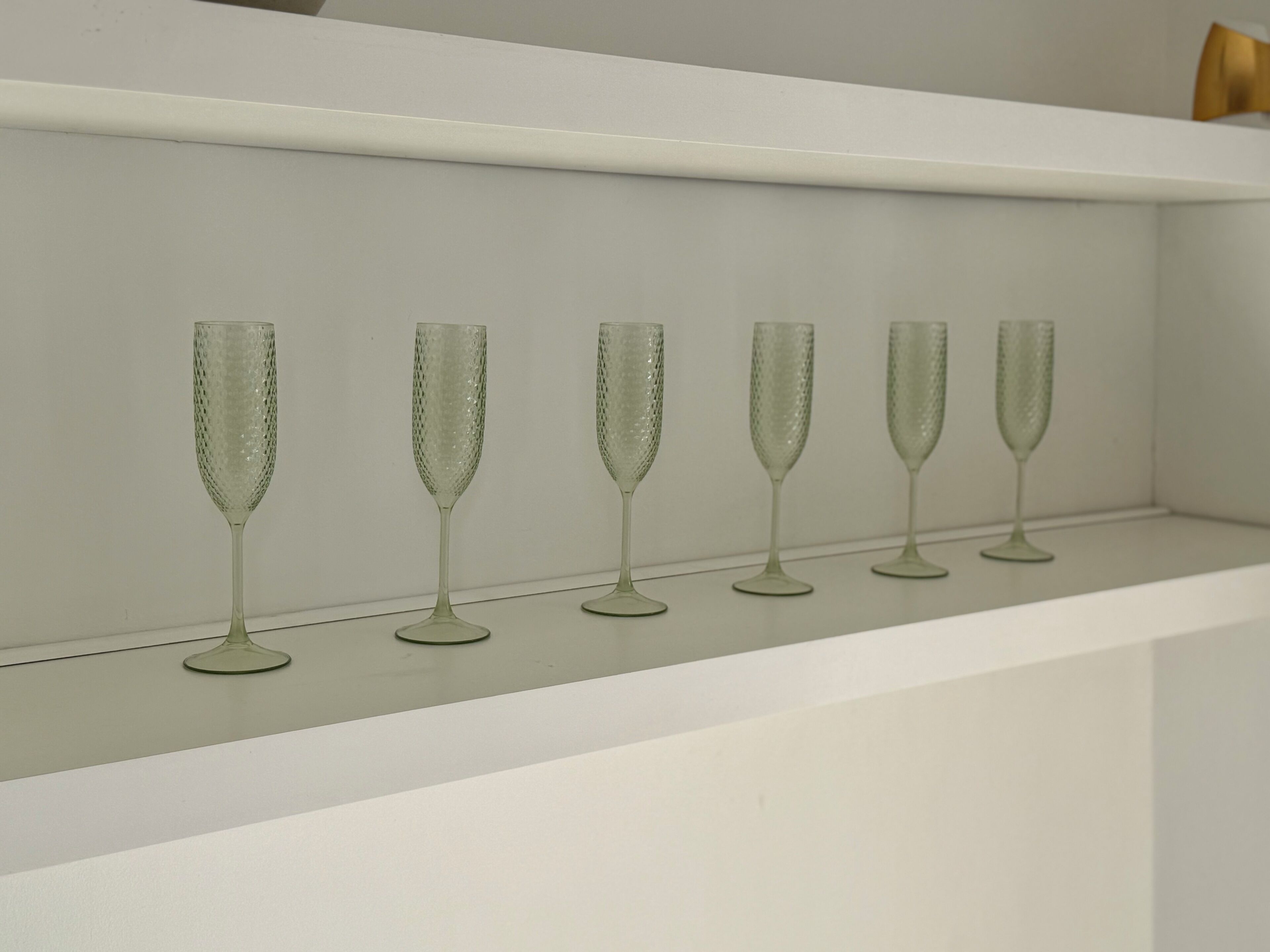A row of five champagne flutes on a white shelf.