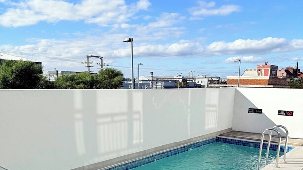 An outdoor swimming pool with a glass barrier, a sign indicating 'Pool Indemnity and Rules', and a clear blue sky in the background. - Chick and Luxurious Studio (Cape Town)