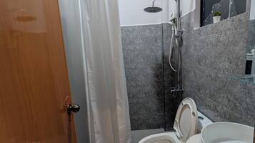 Un baño con ducha, dos inodoros, un lavabo y una planta en maceta.