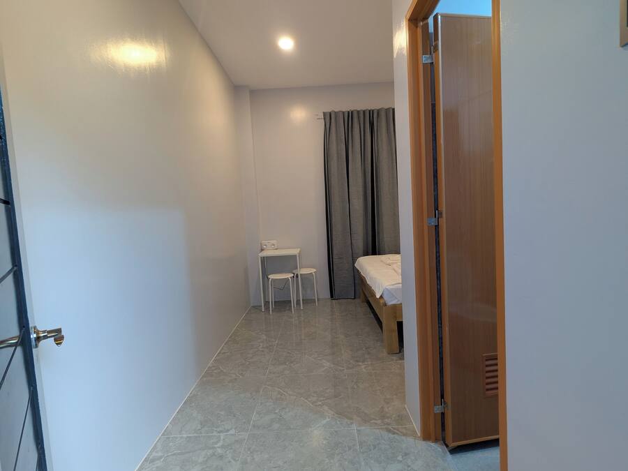 A small, well-lit room with a bed, a desk, and a chair.
