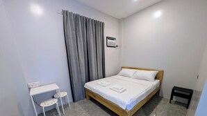 A bedroom with a bed, a small desk with two chairs, a grey curtain, and a wall-mounted air conditioning unit. - The Canyoneer Inn (Alegria)