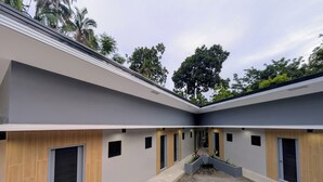 A modern building with a courtyard, featuring a central garden area, multiple doorways, and a mix of grey and wooden paneling. - The Canyoneer Inn (Alegria)