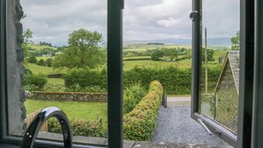 A view from a window overlooking a rural landscape with rolling hills and a stone wall. - Fell View Cottage (Kendal)