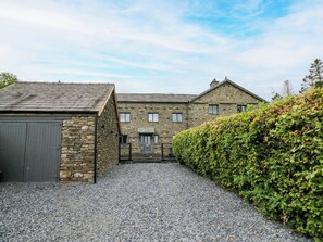 A stone building with a gravel driveway and a hedge.