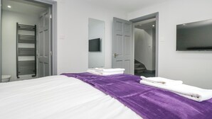 A modern hotel room with a neatly made bed, a purple throw blanket, and a flat-screen TV mounted on the wall. - Fell View Cottage (Kendal)