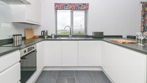A modern kitchen with white cabinets, a black countertop, a window with a colorful valance, a sink, and a toaster. - Fell View Cottage (Kendal)