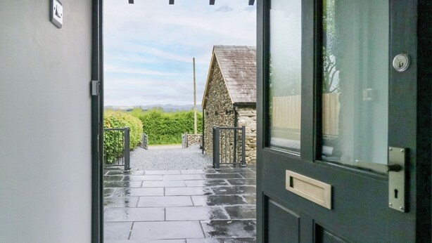 A wet stone pathway leading to a stone building with a metal gate. - Fell View Cottage (Kendal)