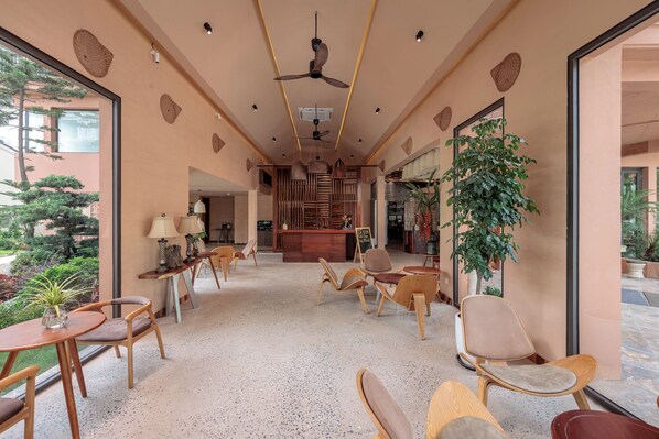 Un espace intérieur vaste et lumineux, agrémenté de meubles en bois, de ventilateurs de plafond et de grandes fenêtres offrant une vue sur l’extérieur.
