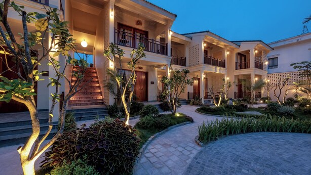 A multi-story hotel with a central courtyard, outdoor lighting, and a staircase leading to the entrance. - La Sen Village (Nam Hoa Lu)