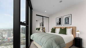 Un dormitorio moderno con una cama grande, una mesita de noche y vistas de la ciudad a través de ventanales del suelo al techo.