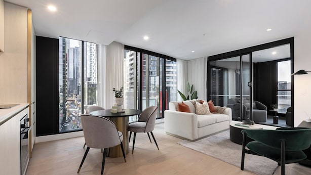 Una sala de estar moderna con un sofá, sillas, una mesita de centro y vistas a un paisaje urbano a través de amplios ventanales.