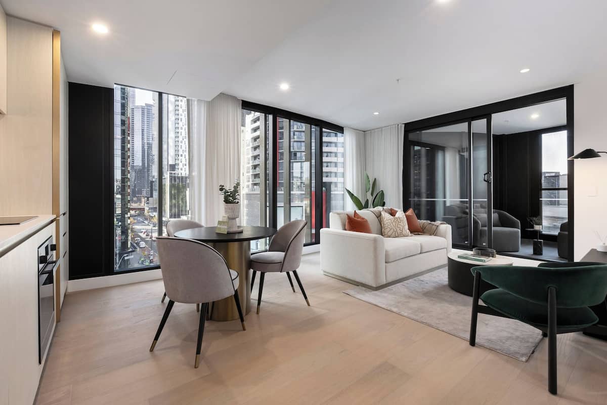 Una sala de estar moderna con un sofá, sillas, una mesita de centro y vistas a un paisaje urbano a través de amplios ventanales.