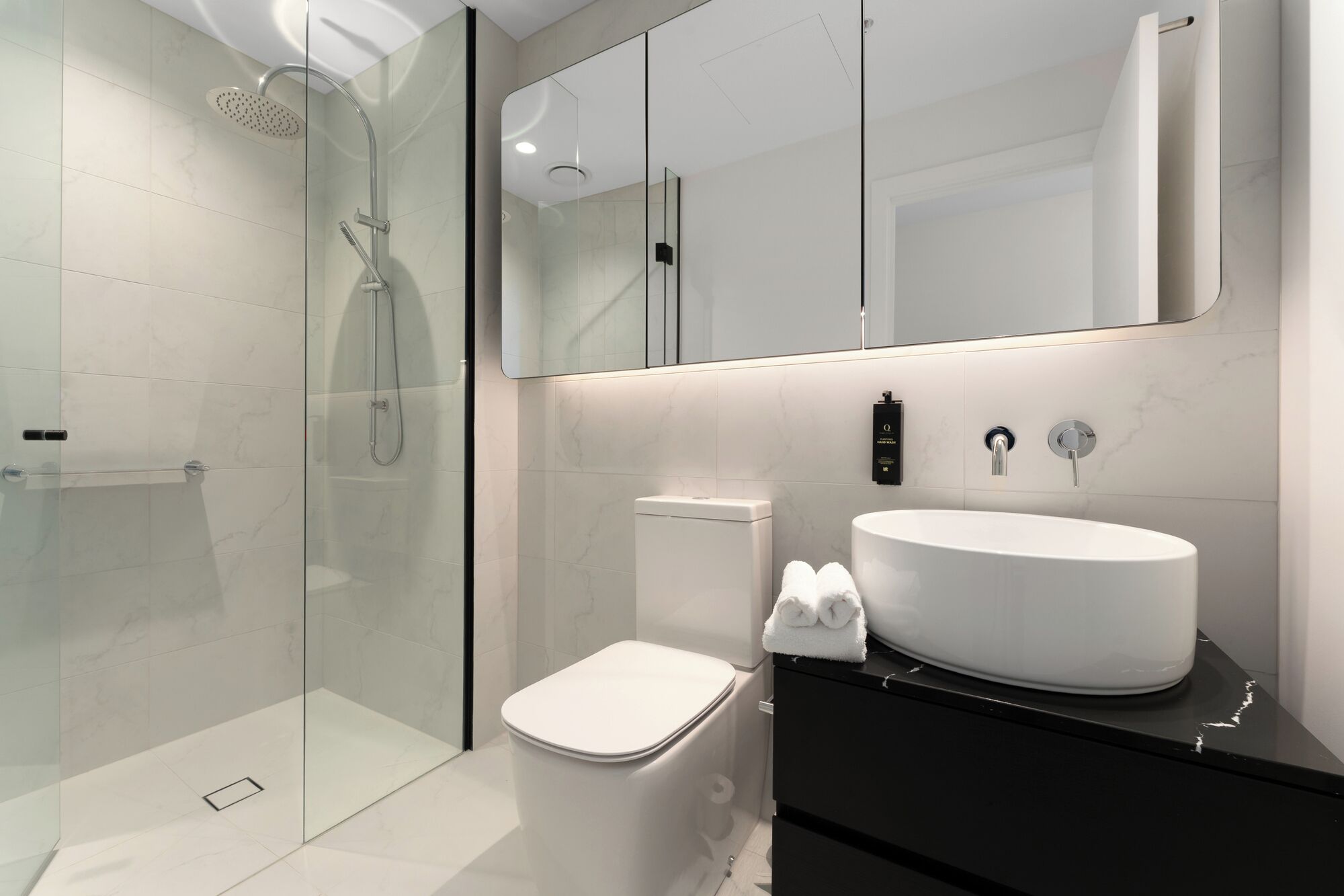 A modern bathroom with a glass-enclosed shower, a white toilet, and a vanity with a large sink.