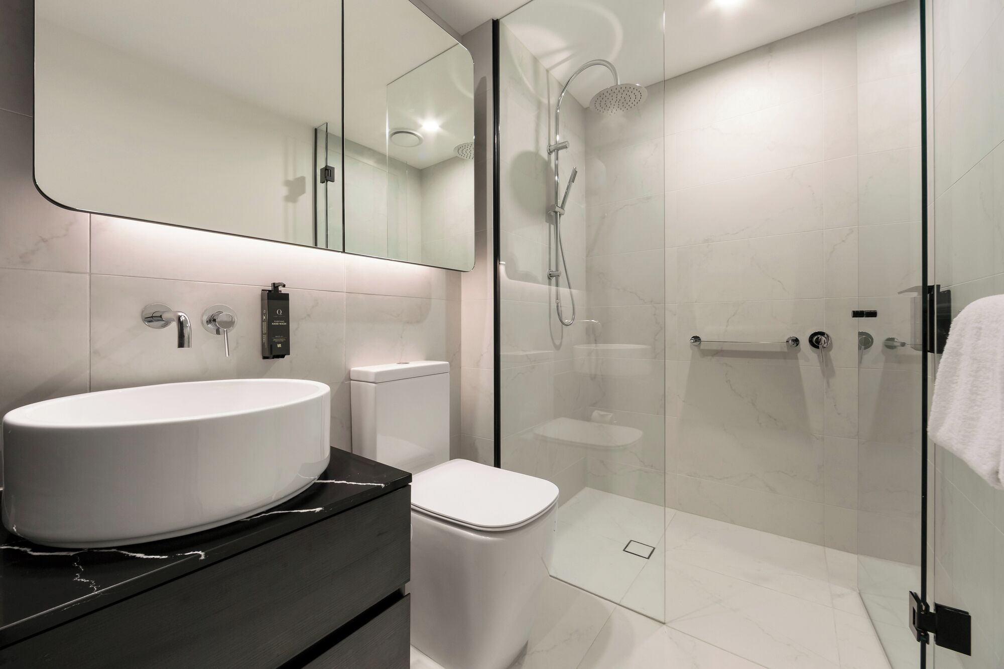 Un baño moderno con ducha de vidrio, lavamanos blanco y retrete.