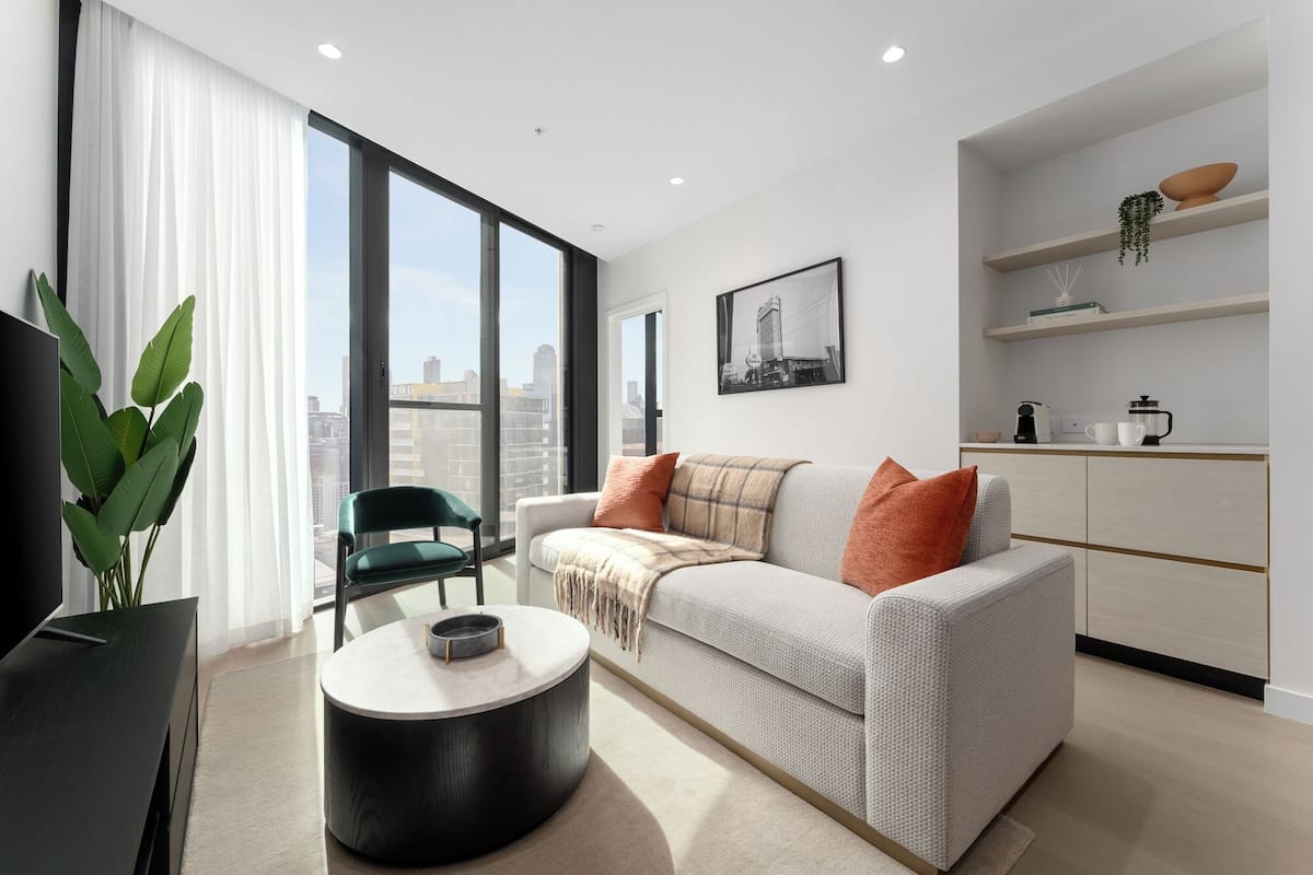 Una sala de estar moderna con sofá, una mesa de centro y vistas de la ciudad a través de amplios ventanales.