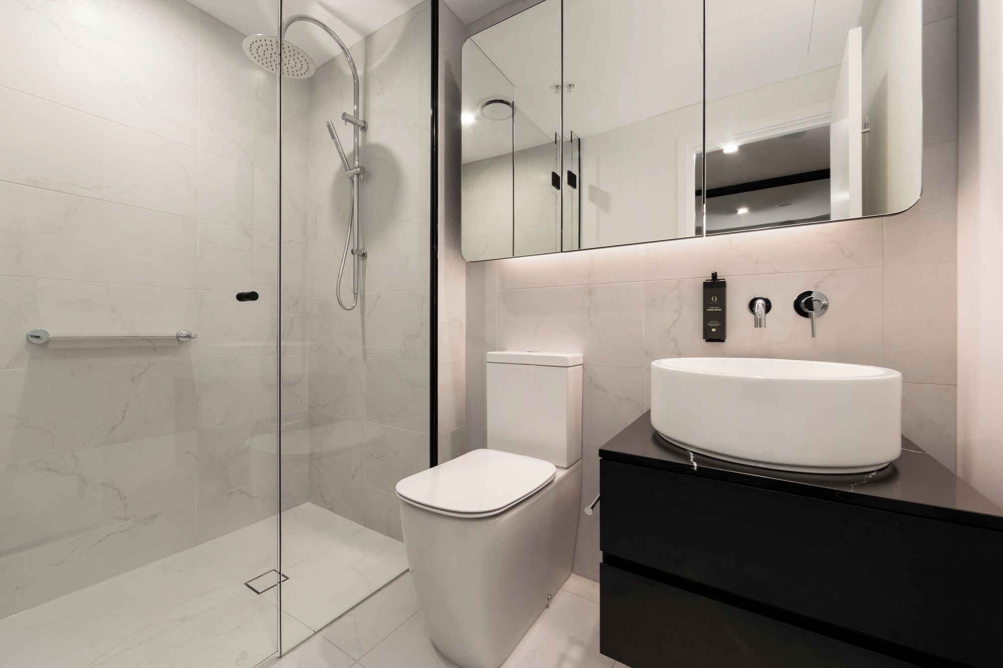 A modern bathroom with a glass-enclosed shower, a white toilet, and a black vanity with a white sink.