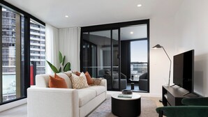 Una sala de estar moderna con un sofá, una mesa de centro, un televisor y vistas de la ciudad a través de amplios ventanales.