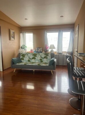 A living room with a sofa, a dining area with a table and chairs, and a kitchen area. - Heart of Downtown Hilo (Hilo)