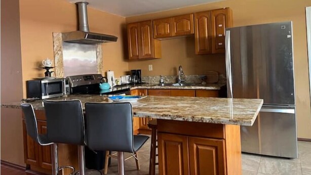 A modern kitchen with wooden cabinets, a stainless steel refrigerator, a microwave, and a gas stove. - Heart of Downtown Hilo (Hilo)