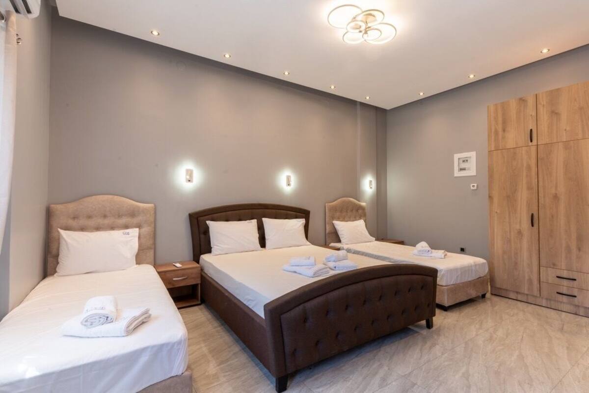 A hotel room with two beds, a wooden wardrobe, and a modern ceiling light fixture.