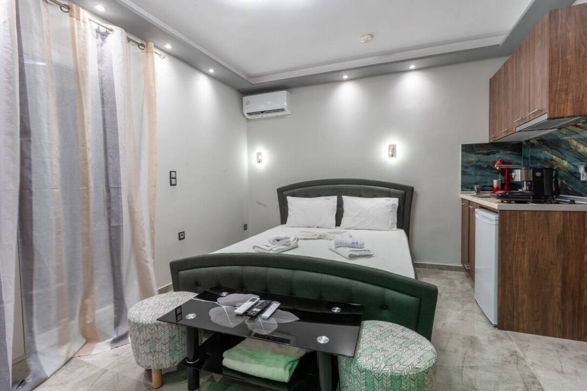 A compact hotel room with a bed, bedside table, and a small kitchenette.