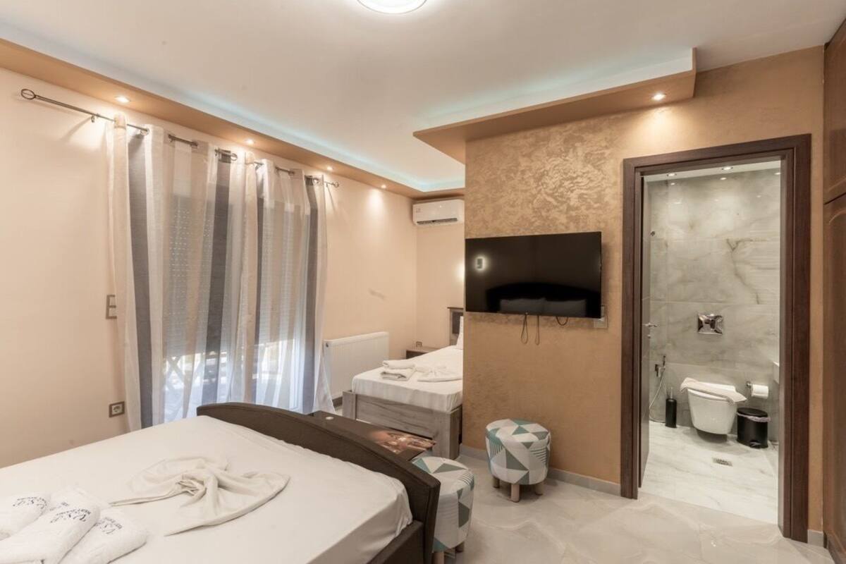 A hotel room with a bed, two bedside tables, a TV mounted on the wall, a bathroom with a shower, and a toilet.