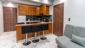 Cocina compacta con armarios de madera, encimera de mármol y barra con taburetes negros.
