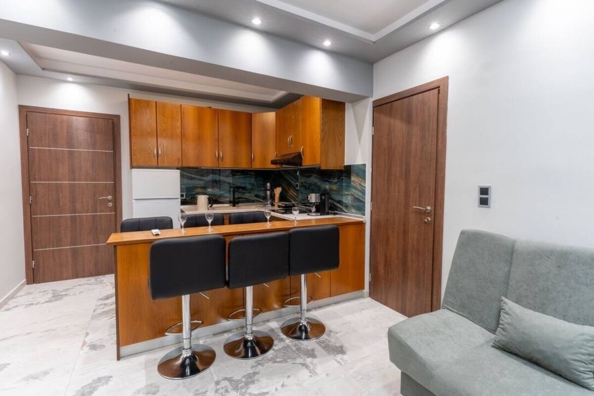A compact kitchen with wooden cabinets, a marble countertop, and a bar area with black stools.
