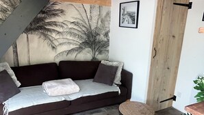 A cozy room with a dark brown sofa, a small round table, and a wooden door. - Maisonnette and terrace in the heart of the village to do everything on foot in St Mandrier (Saint-Mandrier-sur-Mer)