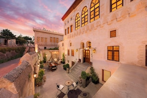 A courtyard with a dining area, outdoor seating, and a building with multiple windows and a staircase. - Akantha House (Urgup)