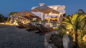 Un complexe hôtelier doté d’une piscine, de chaises longues, de parasols et d’un grand bâtiment avec de nombreux balcons.