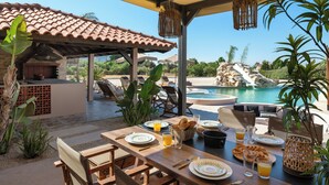 Un espace extérieur aménagé pour les repas, avec une piscine, des meubles en bois et des plantes tropicales.