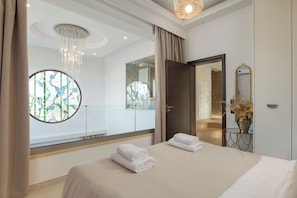 Una camera d'hotel moderna con un letto grande, uno specchio rotondo, un lampadario e vista sul balcone esterno.