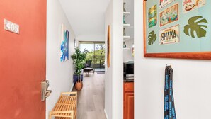 A hallway with a number sign, a bench, a plant, and a view to a balcony with outdoor seating.