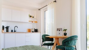Cocina pequeña con armarios blancos, encimera de madera y zona de comedor con dos sillas verdes.