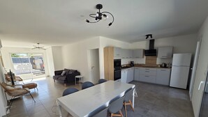 Ett modernt kök med en central köksö, vita skåp och en matplats med stolar.