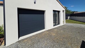 En modern byggnad med en stor garageport, ett litet fönster och en övervakningskamera.