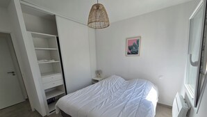 Ett sovrum med en säng, en garderob, ett nattduksbord, en lampa och ett fönster.