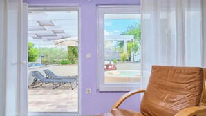 Une pièce dotée d’une porte-fenêtre coulissante donnant sur un espace extérieur avec une piscine, des chaises longues et une table.