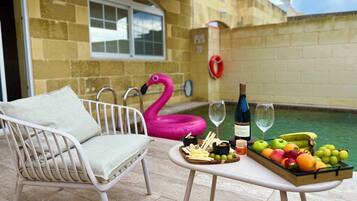 Ein Poolbereich mit weißem Stuhl, einem Flamingo-Schwimmtier, einem Tisch mit Früchten, Käse und Weingläsern.