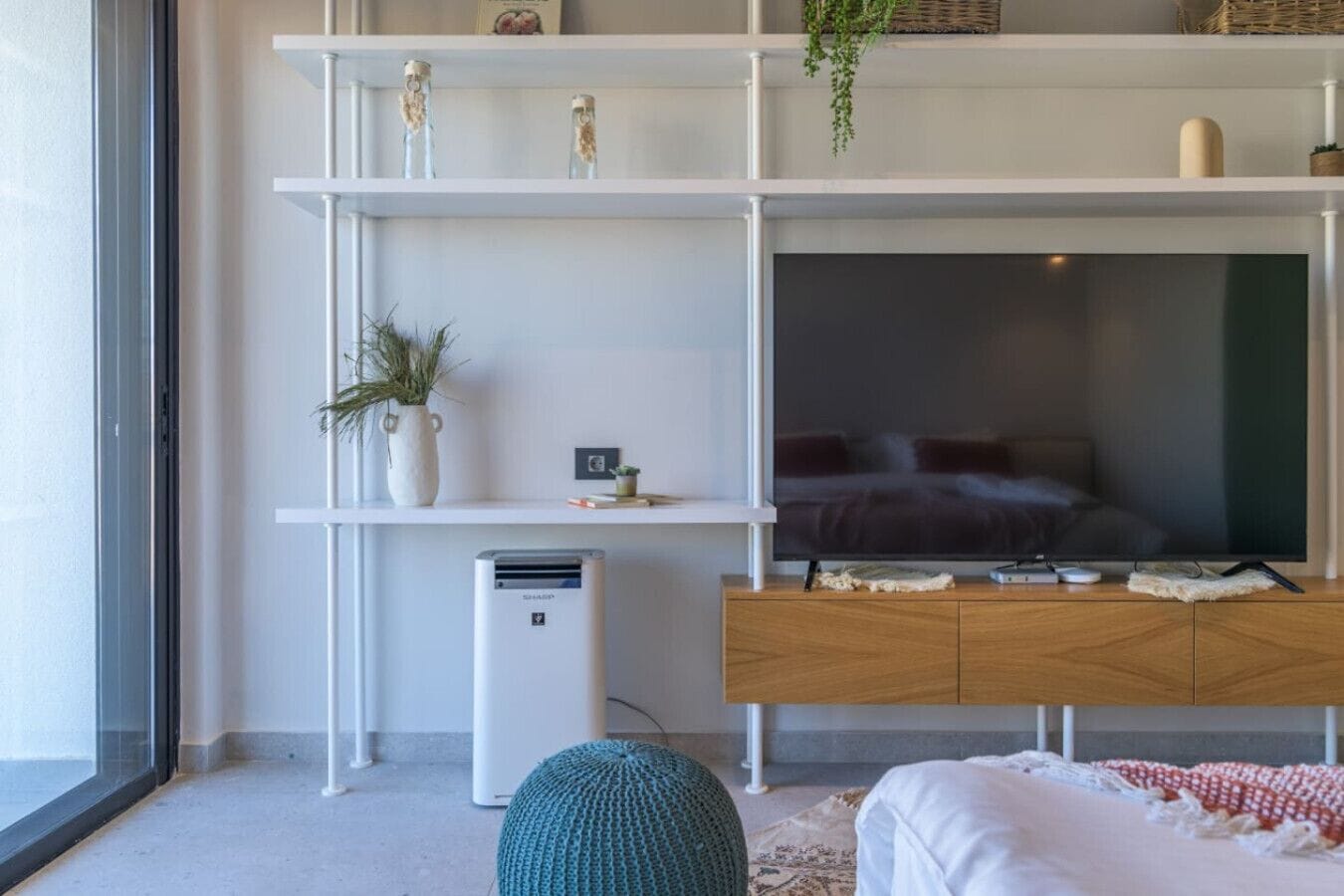 Una sala moderna con un televisor de pantalla plana grande, armarios de madera y una estantería blanca con adornos.