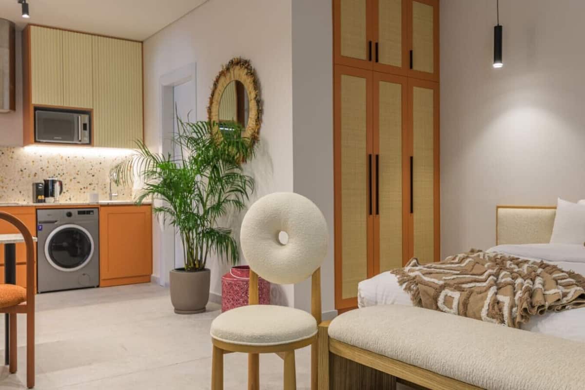 A modern bedroom with a bed, a chair, a washing machine, a potted plant, and a wardrobe.