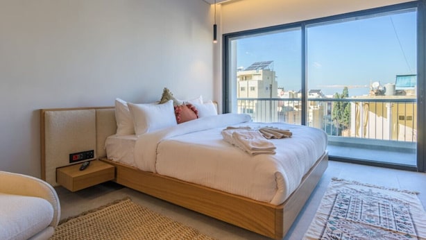 Un dormitorio moderno con una cama grande, una mesita de noche con un control remoto y vistas a la ciudad a través de un ventanal.