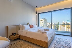 A modern bedroom with a large bed, a bedside table with a remote control, and a view of the city through a large window. - BOHO Studios by Stayinn (Beirut)