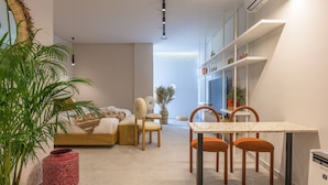 Una sala moderna con un sofá, sillas, una mesa de comedor y una zona de cocina con estantes y un televisor.