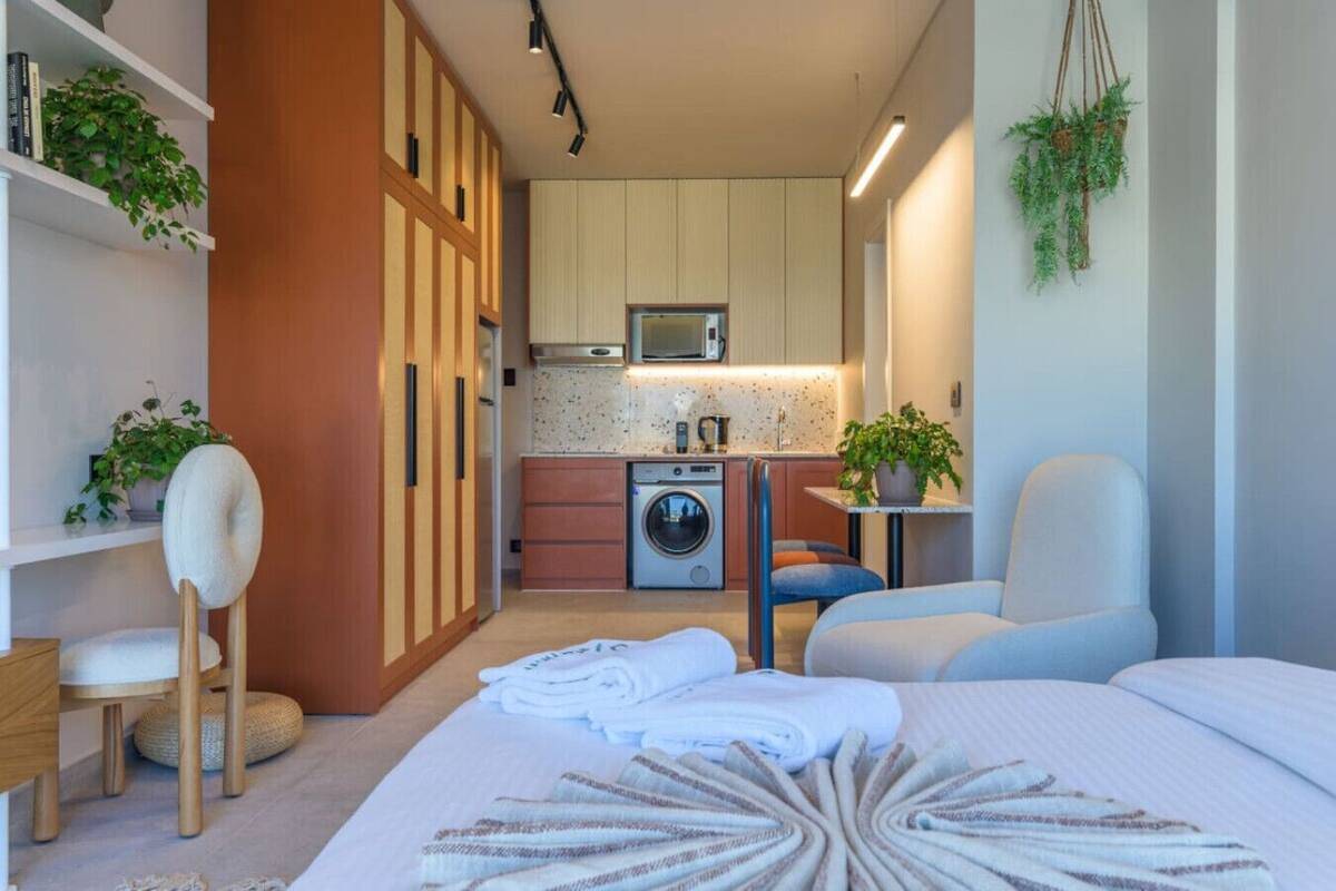 A compact living space with a kitchenette, a washing machine, a dining area, and a bed with neatly folded towels.